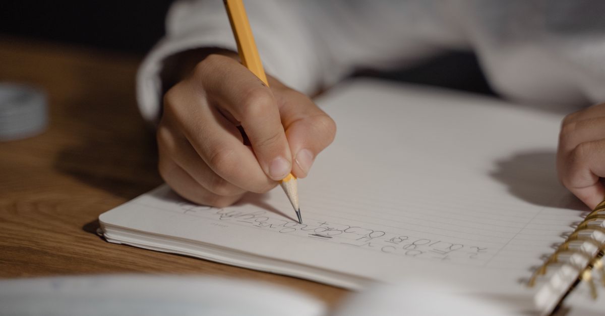 Close-up of a child writing homework using a pencil on a spiral notebook. Ideal for education themes.